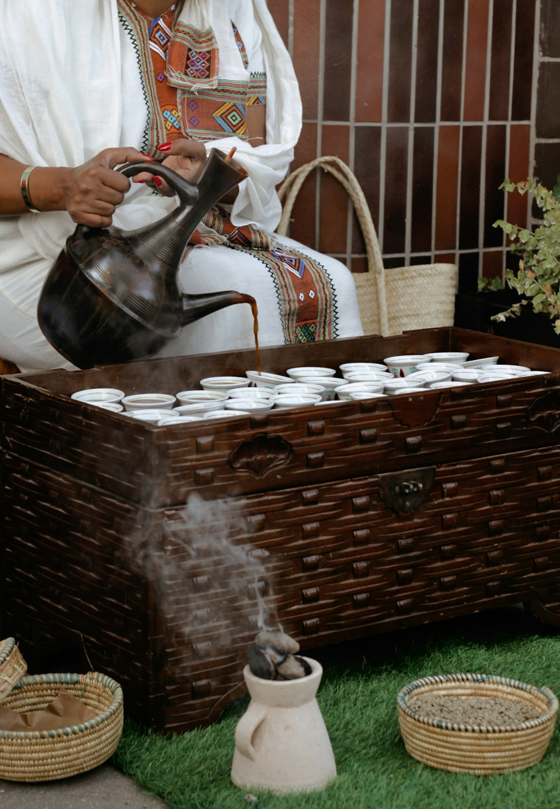 Ceremonie du cafe ethiopienne : femme en tenue traditionnelle versant le cafe d'une jebena dans de petites tasses