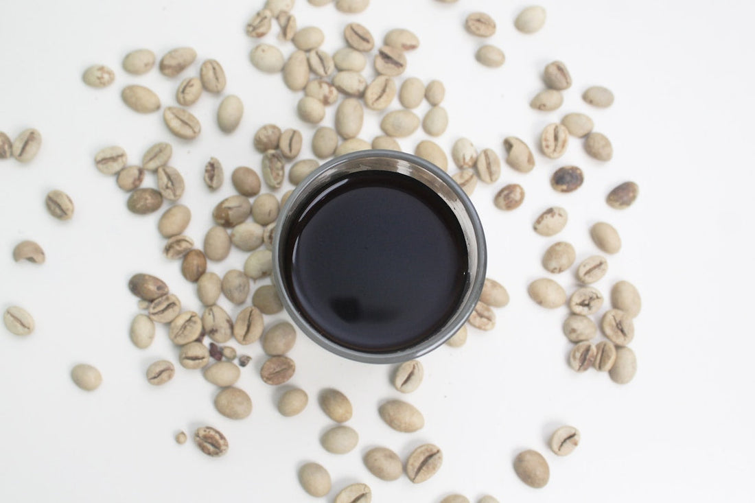 Tasse d'espresso robusta noir intense entouree de grains de cafe verts non torrefies sur fond blanc